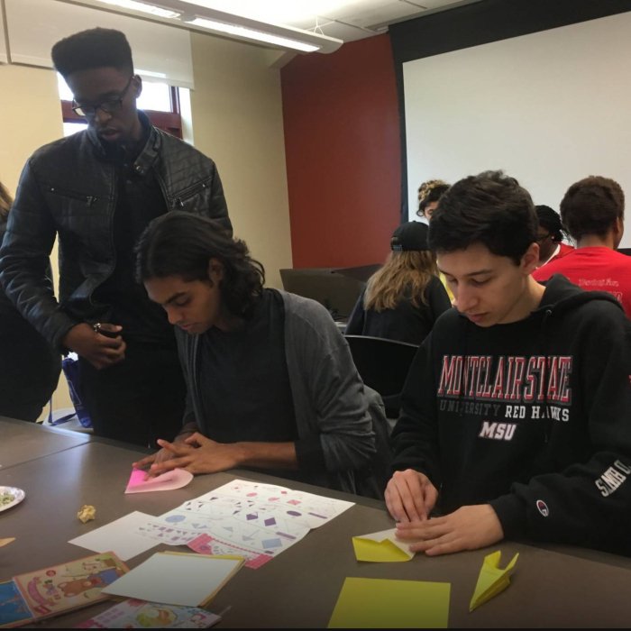 Two college students fold origami as another student watches them