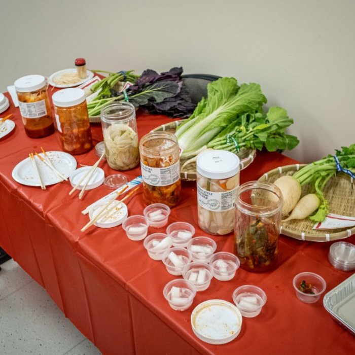 A table is set with bowls of vegetables, seasonings, and other cooking ingredients for a cooking demonstration