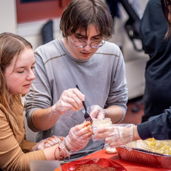 Two college students use a fork to pick ingredients from a jar