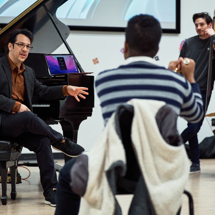 Oscar Perez Jazz Studies Coordinator talks to students sitting at piano
