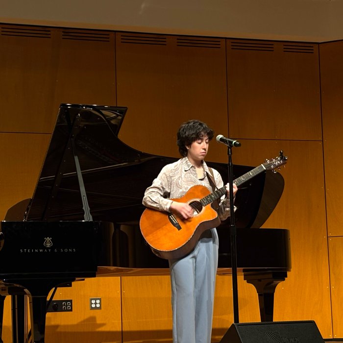 Guitar performer on stage with piano behind