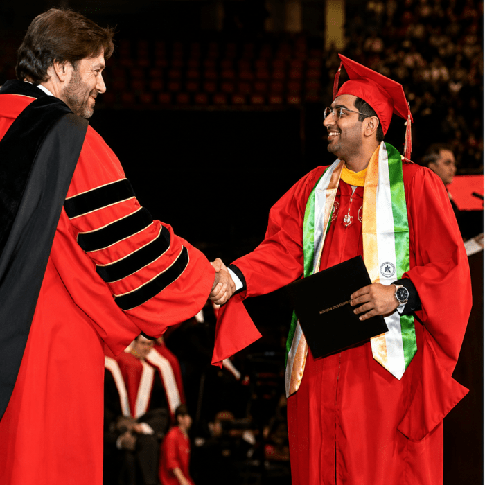 A picture of a student shaking hands with President Koppell at graduation. Both are wearing regalia.