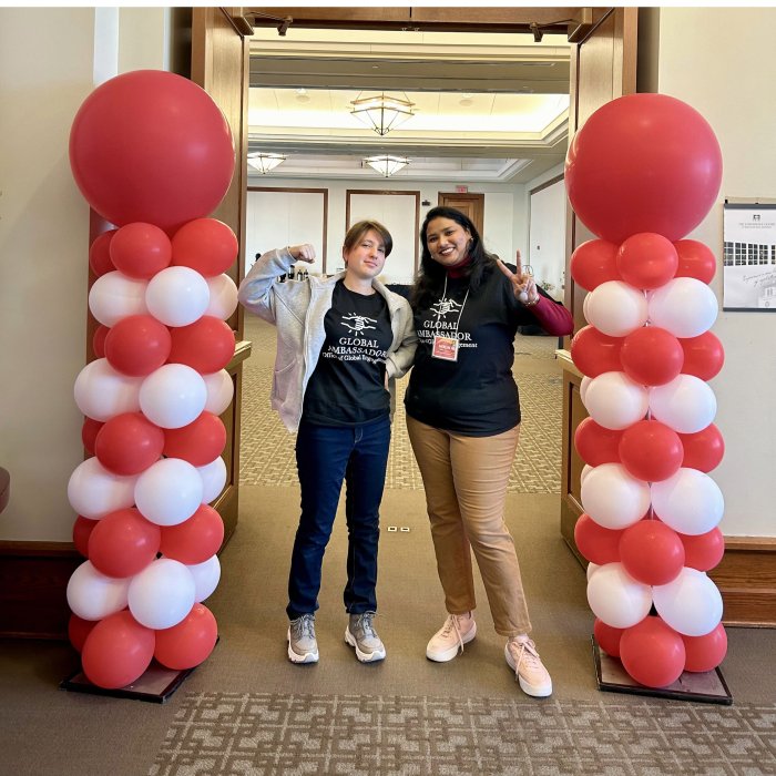 A picture of two global ambassadors standing next to two towers of red and white balloons.