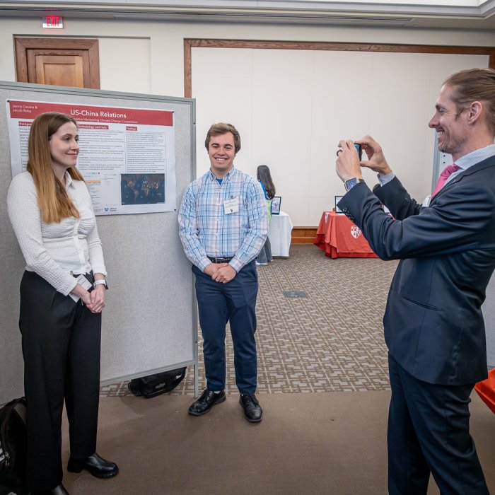Students smiling next to their poster for a photo