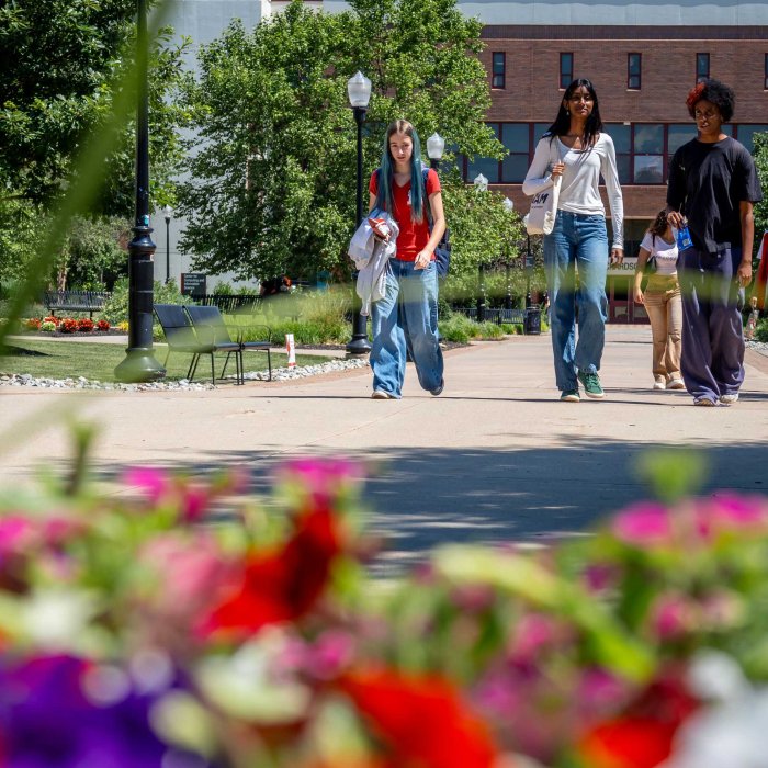 Three students walking toward the camera at Montclair State University, with flowers in the foreground.