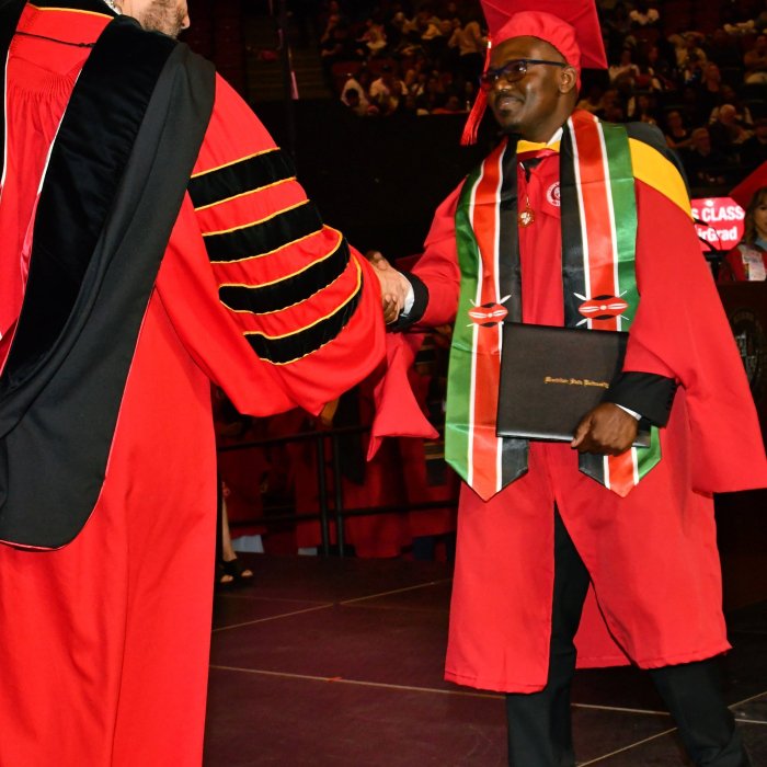 Victor Owino graduation picture. Student is shaking hands with President Koppell