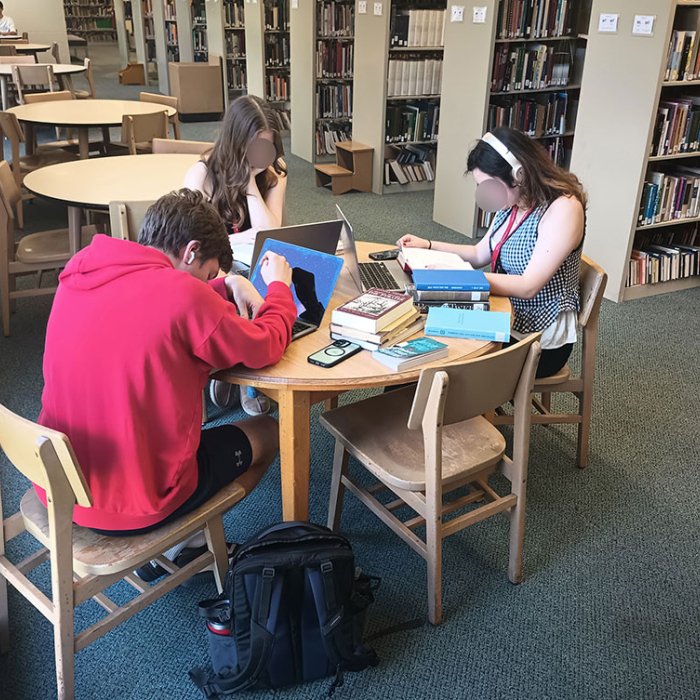 3 students sitting at a table on laptops