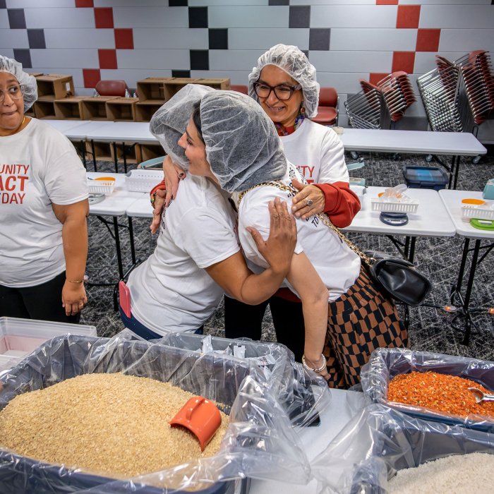 Employees embrace while bagging food on Community Impact Day.