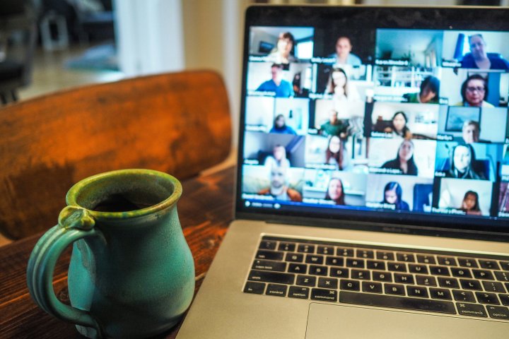A coffee cup sits next to a laptop open with Zoom participants. 