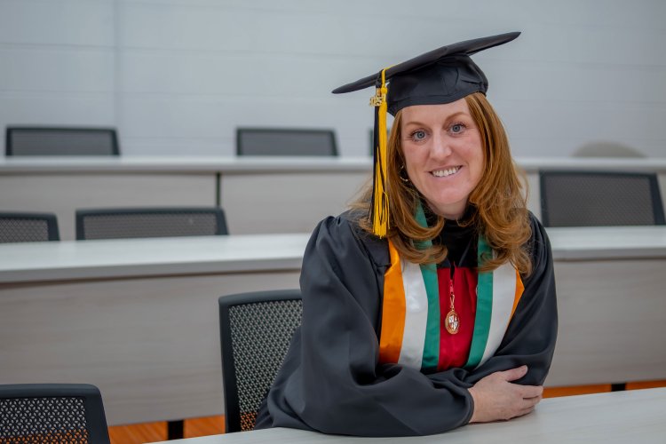 Jean-Marie Beeks sits in a classroom in her graduation cap and gown.