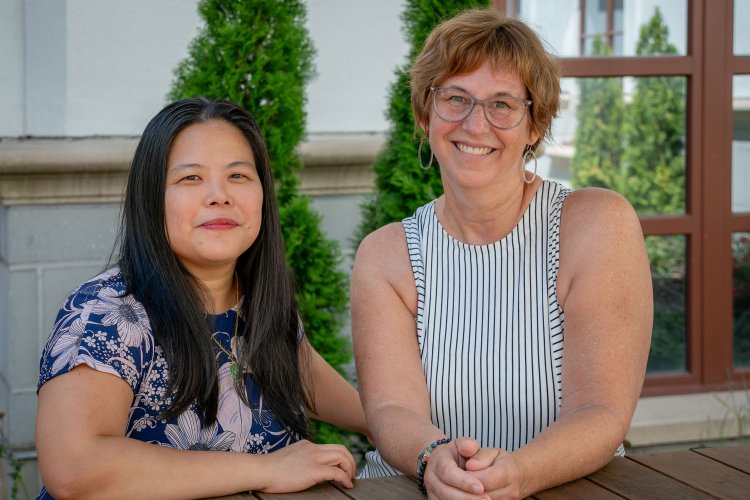 Two women stand side by side in a courtyard on the Montclair State University campus.
