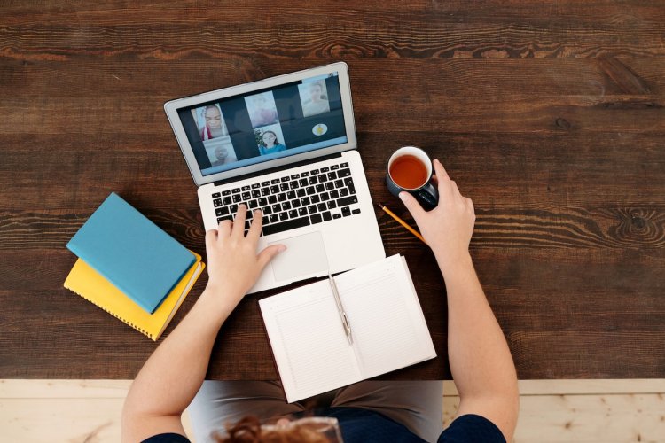 person sitting at computer with open notebook and a tea