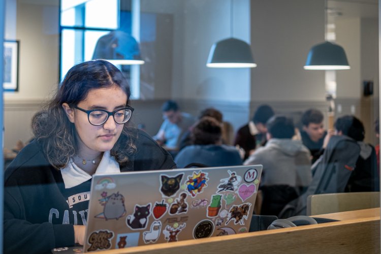 Student studying on her laptop in a crowded cafe on campus.