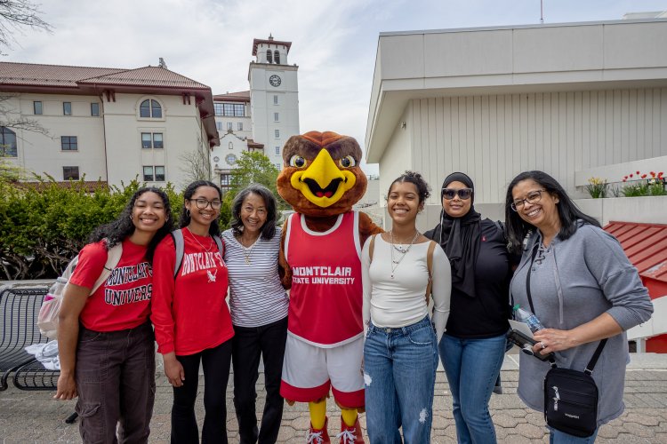A family taking a group picture with the mascot, Rocky the Red Hawk