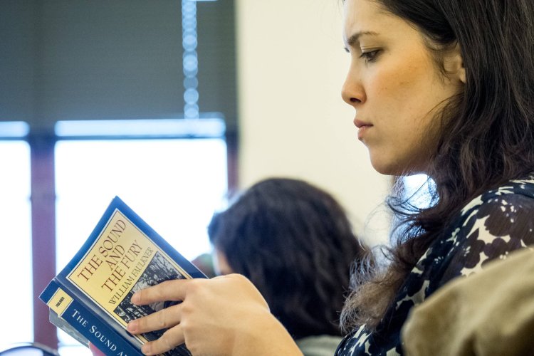 Student reading a copy of the Sound and the Fury in a classroom