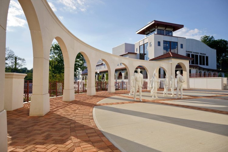 Late-day view of an arched promenade with long shadows and a nearby statue installation.