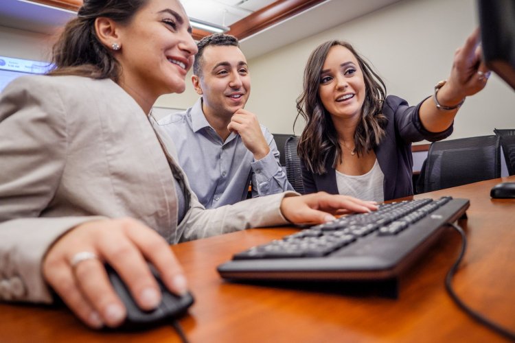 A group of three students sit around a computer and study the screen