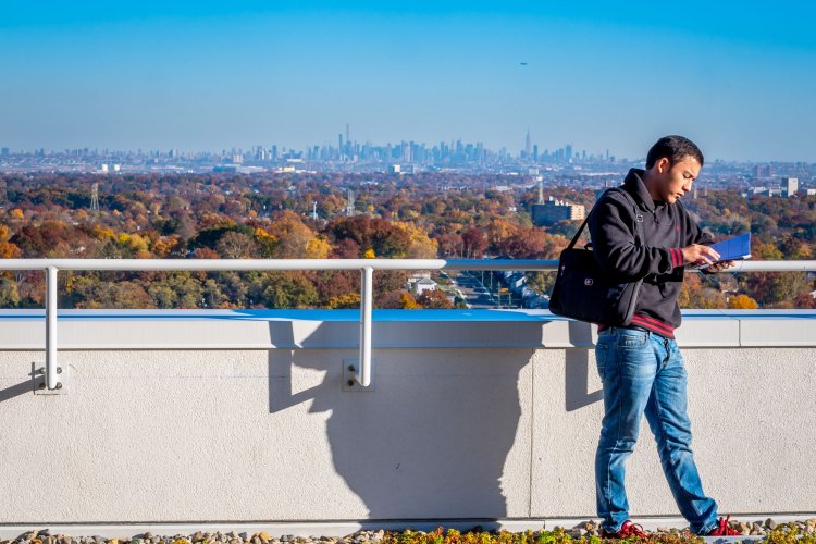 A student reads a book and leans against a wall overlooking North Jersey and New York City