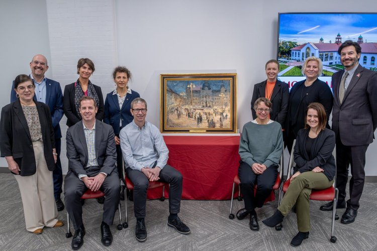 A group of people pose around a framed painting 