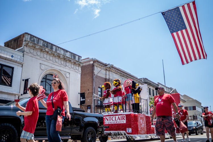 Individuals walking in parade procession around Montclair float, American flag above