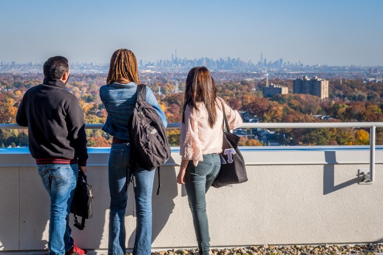 Three people stand with backs to camera looking at New York City skyline from Montclair's campus