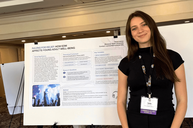 Student stands in front of her research project on display.