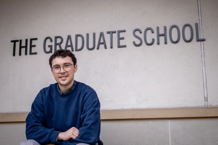 Student sitting in front of The Graduate School sign
