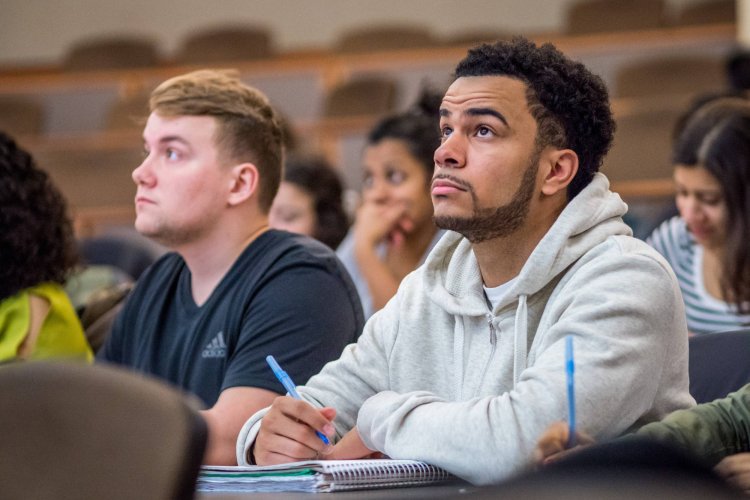 Two college students sitting in a classroom, taking notes during a lecture