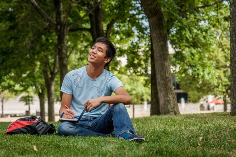 A college student sits in a grassy field and focuses his attention to the sky