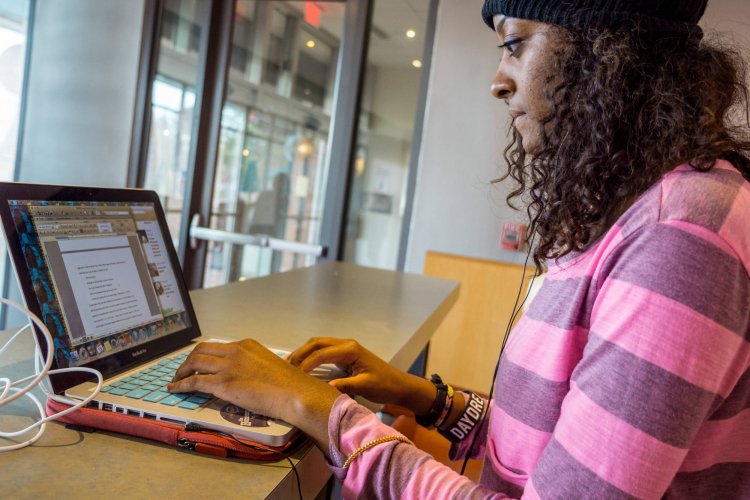 A college student sits at a table and types on a laptop