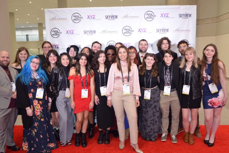 Students pose with faculty supervisor Anabella Poland in front of step=and-repeat.