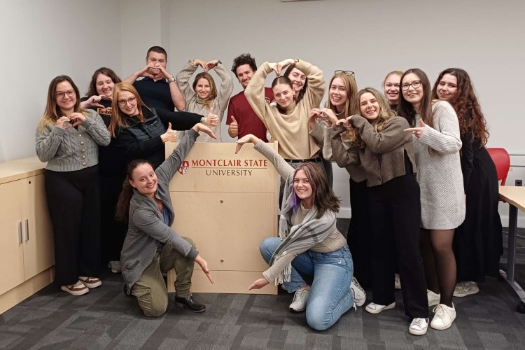 A group of people pose around a podium and point to the "Montclair State University" logo on it