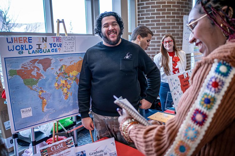A man stands in front of a map at a booth and smiles at a visitor