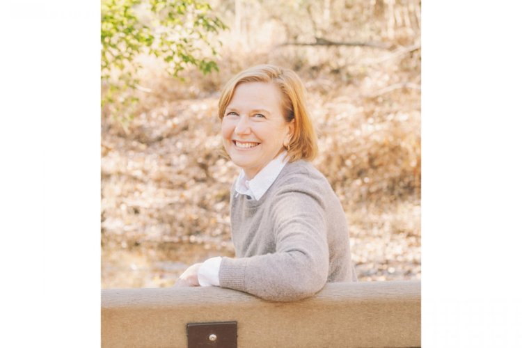 Portrait of a woman wearing a tan sweater seated on a bench in a park