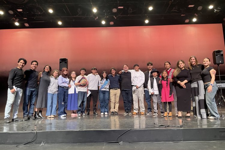 A group of college students and professors stand in a half-circle on a stage