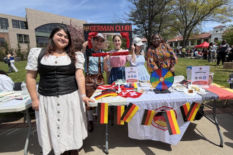 Five college students pose in front of a decorated booth for the German Club
