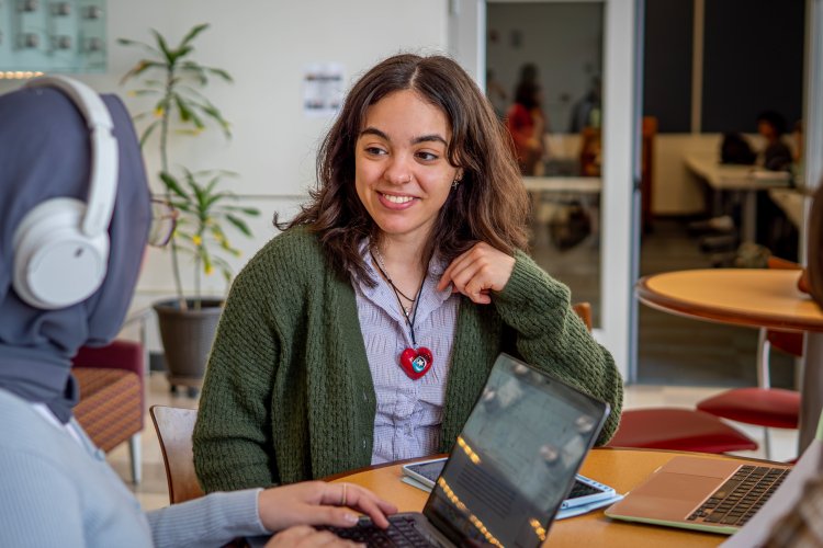 Two students talking, one on a laptop