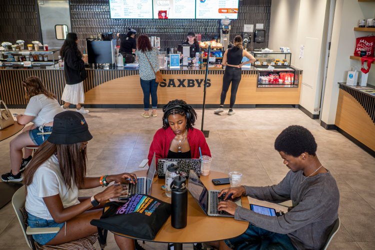 Three students sitting at a table on laptops in a cafe. 