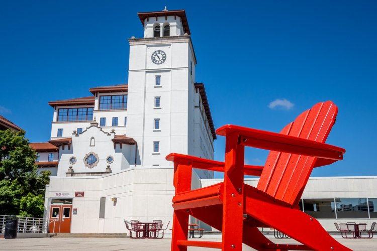 Campus in the summertime with a red chair and building in the background.