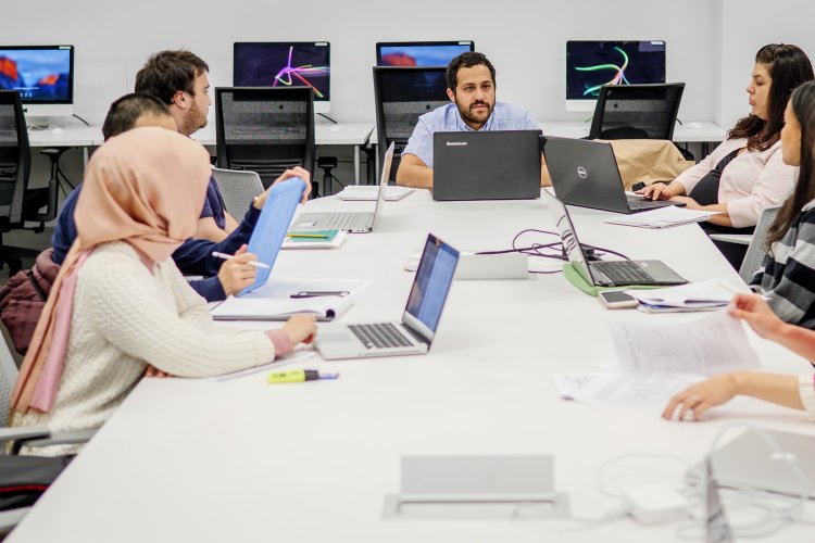 Students working on their computers at a long table.