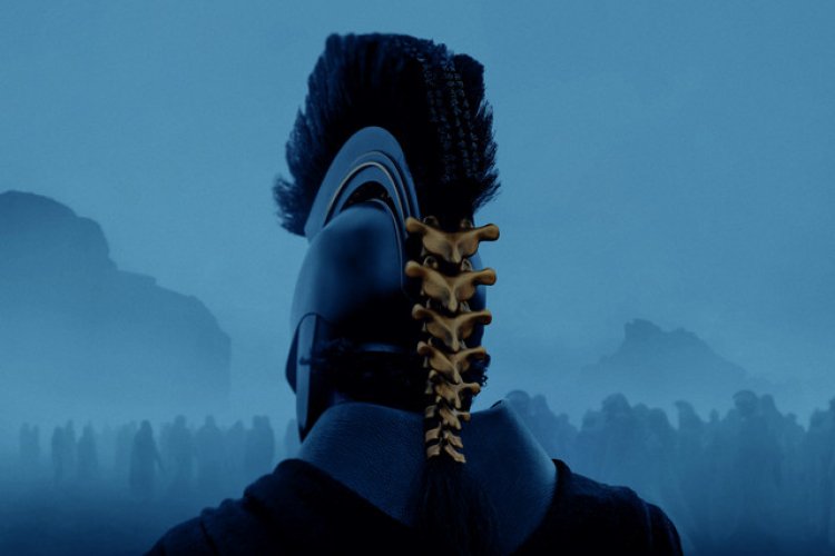 Man in helmet with gold spine on the back of his head riding into war. It is dark and foggy and you can see the outlines of the mountains ahead. 