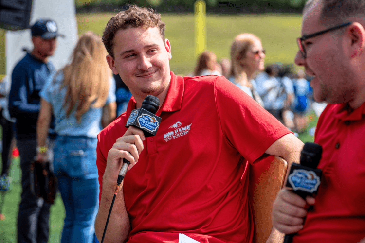 Student holding mic listening to another student on his right speaking at the Yogi Berra stadium.