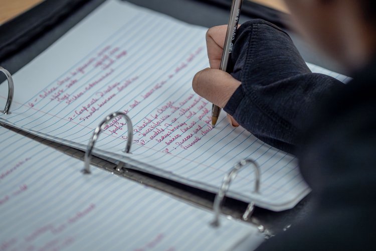 Student writes down notes in a binder.