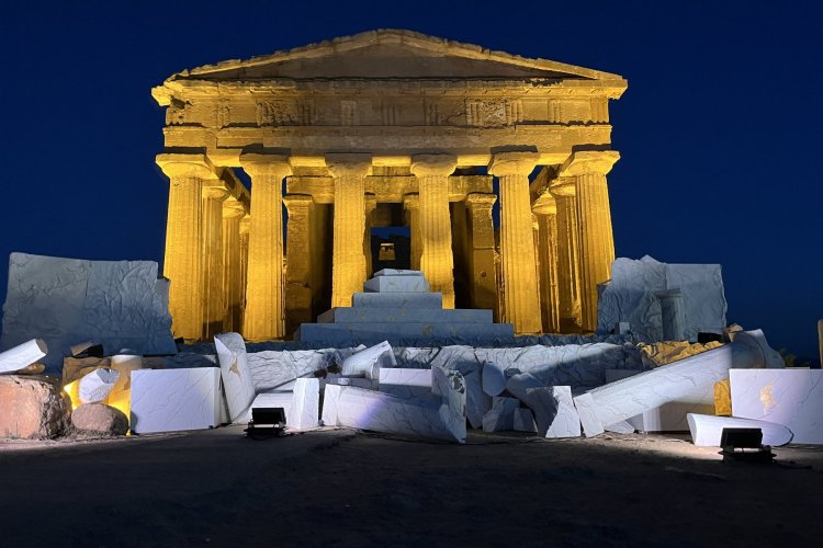 A performance stage at night with fake crumbled marble ruins and an image of the Parthenon behind it 
