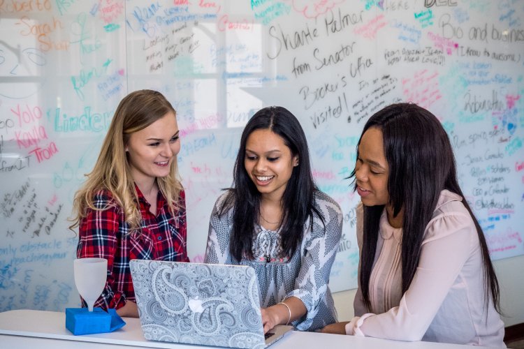 Three students working on laptop in front of whiteboard
