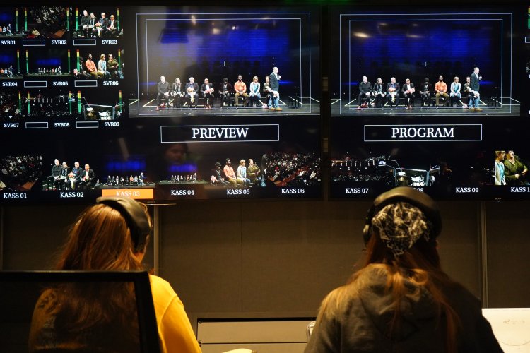 Two people working on a TV production project, wearing headphones and looking at monitors, with their back to the shot.
