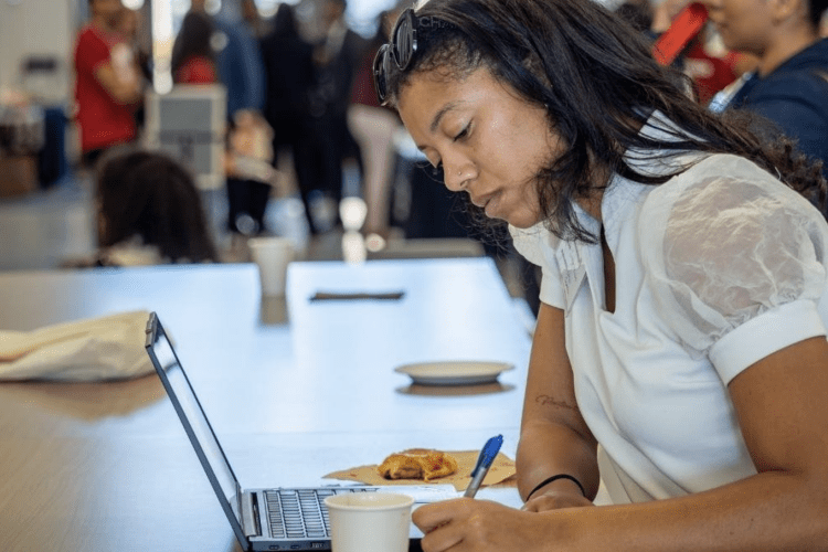 woman sitting with her laptop and coffee writing something down