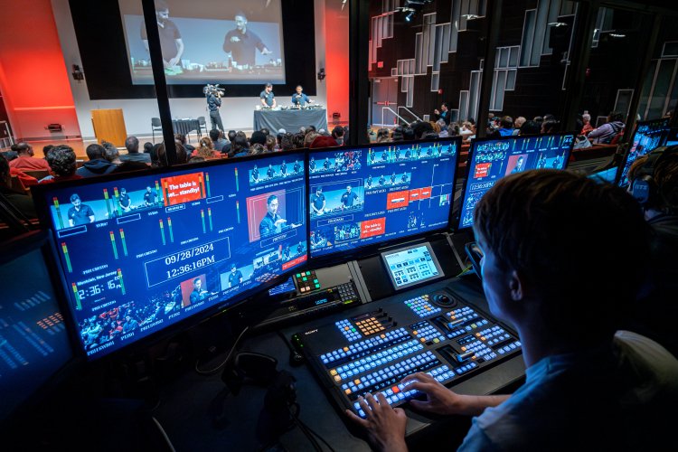 A student in front of several TV production monitors, controlling audio and visual elements of a show.
