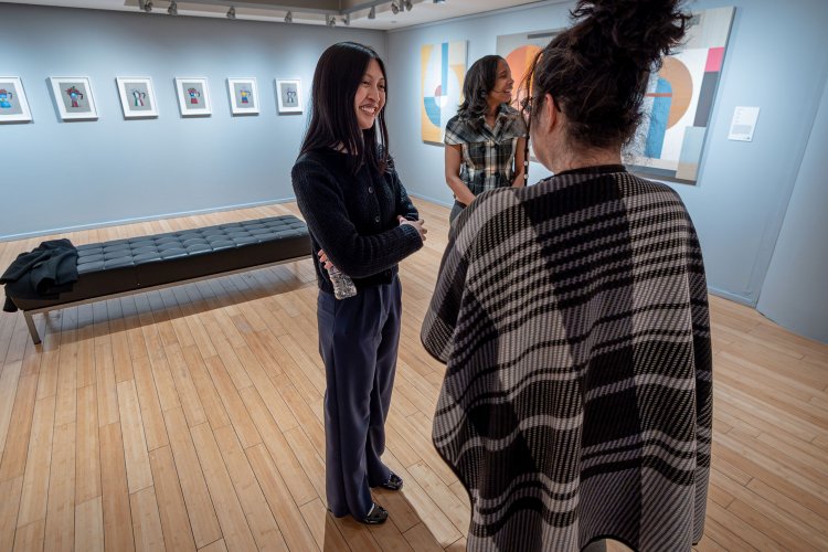 Three people smiling and talking in an art gallery.