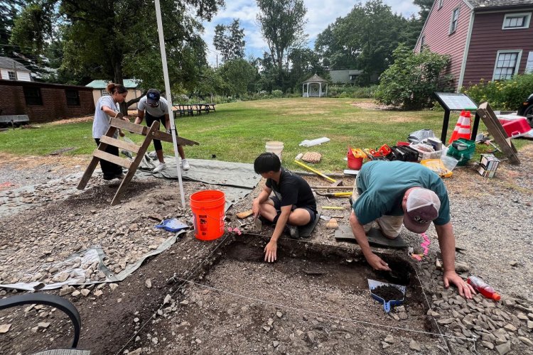 Two people kneel over a hole in the ground and sift through the soil